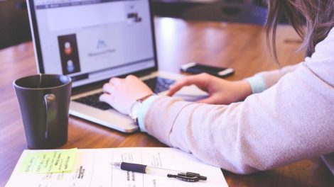 Persona trabajando en un portátil sobre un escritorio con notas y una taza.