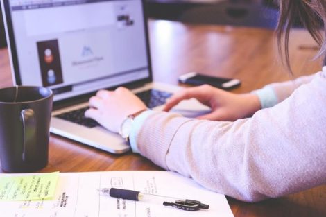 Persona trabajando en un portátil sobre un escritorio con notas y una taza.